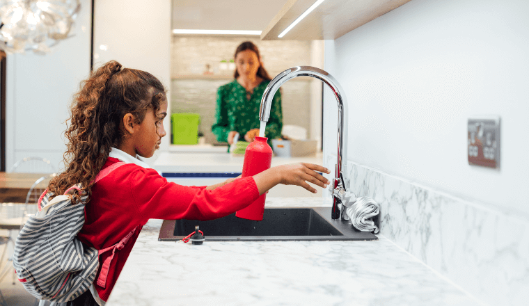 Girl filling up water bottle at kitchen sink